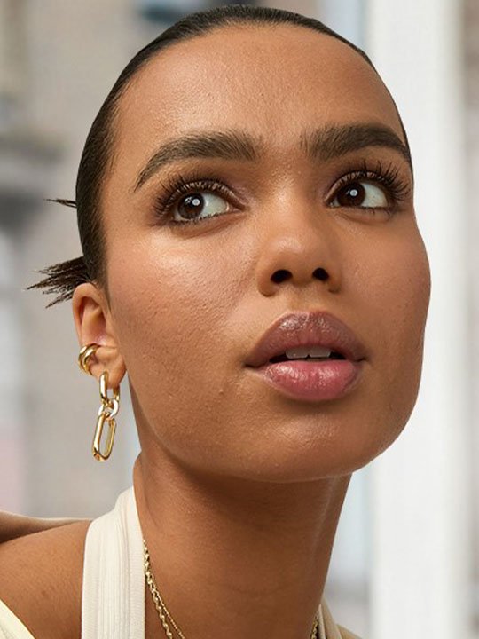 Nahaufnahme eines Gesichts mit natürlichem Look, voluminösen Wimpern und goldenen Ohrringen.