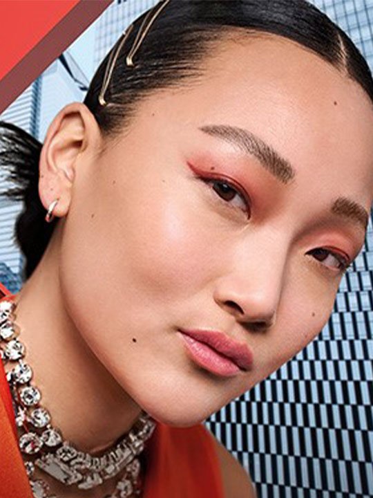 Frau mit rotem Lidstrich und Schmuckkette vor urbanem Hintergrund – betontes Augen-Make-up und Statement-Look.