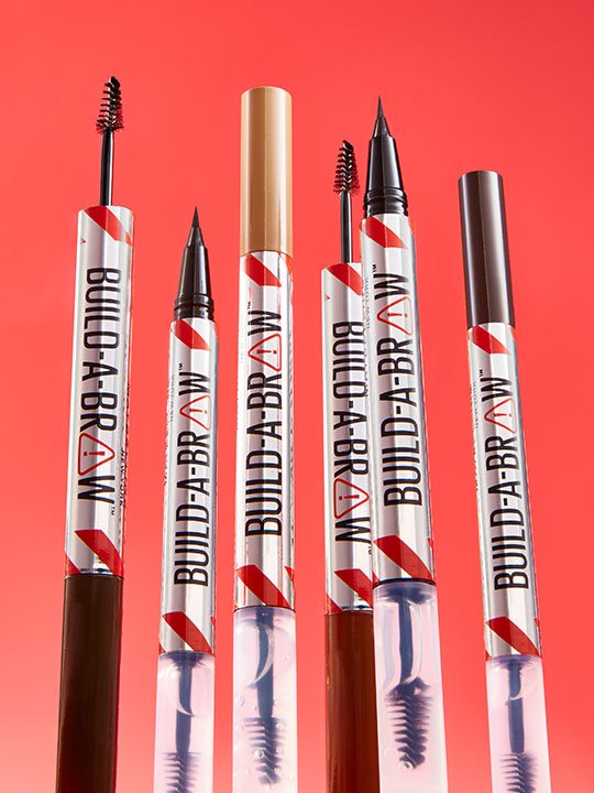 Produktfoto verschiedener Build-A-Brow Augenbrauenstifte in unterschiedlichen Varianten auf rotem Hintergrund.