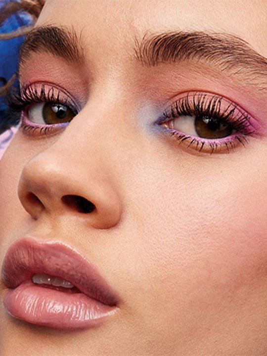 Nahaufnahme eines Gesichts mit farbenfrohem Lidschatten in Pink und Blau sowie stark betonten, voluminösen Wimpern.