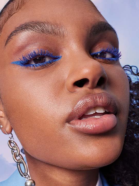 Trendiger Beauty-Look mit kräftig blauer Mascara, Eyeliner und glossy Lippen – Nahaufnahme einer Frau mit dunklem Teint.