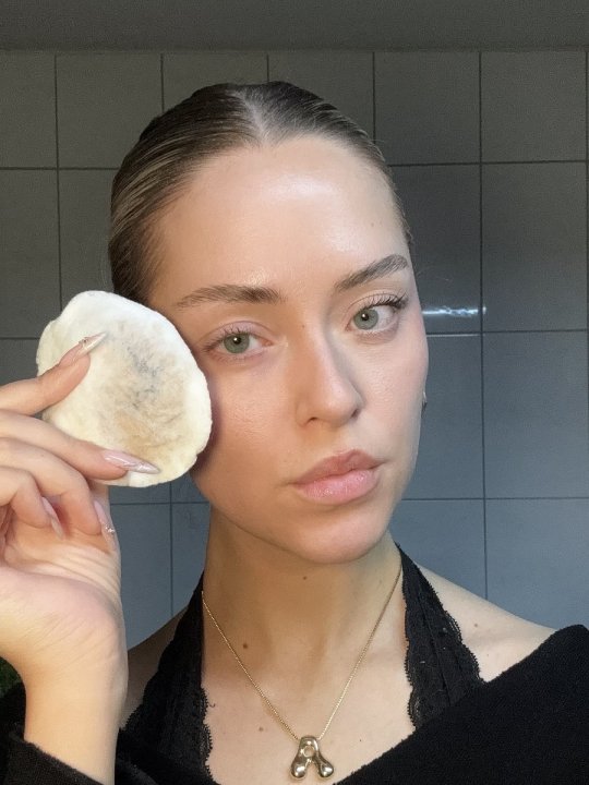 Profilbild einer Frau, die auch dem Abschminken ein benutztes Wattepad neben ihr Gesicht hält