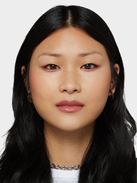 Porträt einer jungen Frau mit schwarzen Haaren, braunen Augen vor weißem Hintergrund.