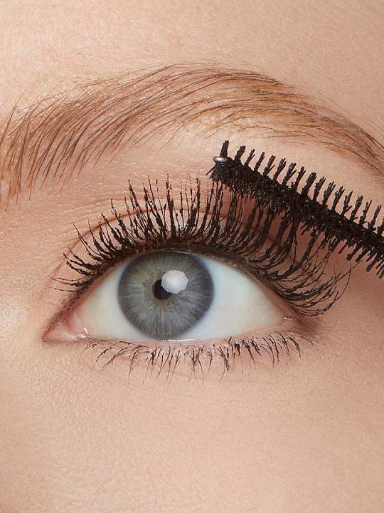 Nahaufnahme eines blauen Auges einer Frau, die sich ihre Wimpern mit Tubing Mascara schminkt