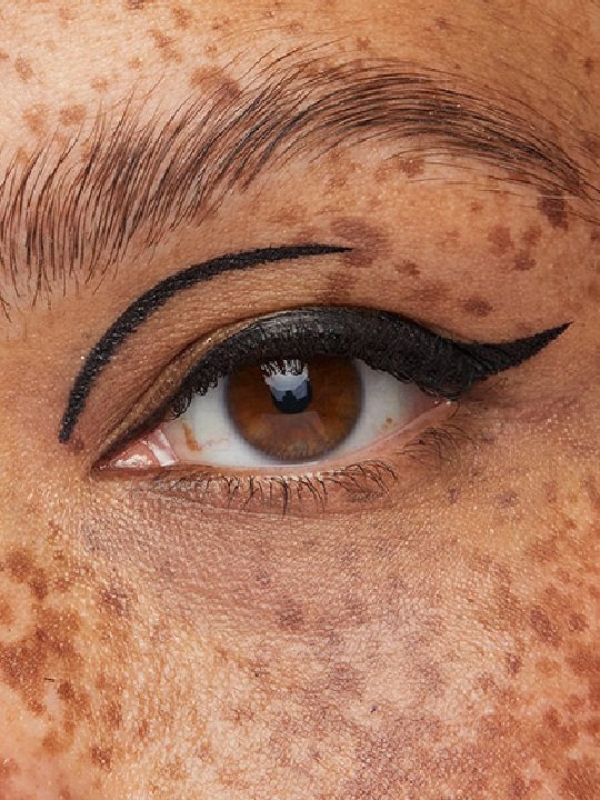 Nahaufnahme eines braunen Auges mit schwarzem Eyeliner entlang des Wimpernkranzes und entlang der Lidfalte bis zur Mitte des Augenlids