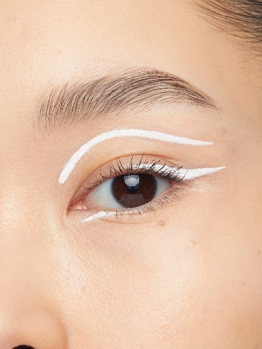 Nahaufnahme eines Auges mit weißem Eyeliner entlang des oberen und unteren Wimpernkranzes sowie entlang der Lidfalte