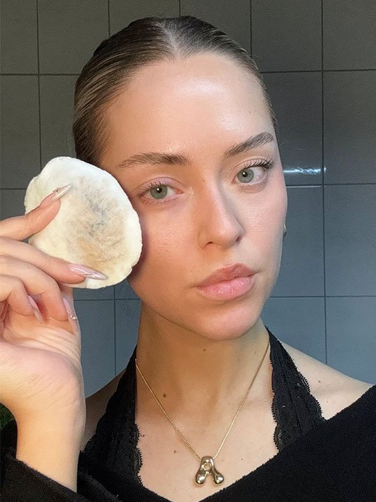 Frau entfernt Make-up mit einem Wattepad, zeigt reine Haut im Badezimmerlicht.