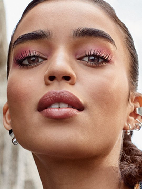 Frau mit dramatischem Make-up, betontem pinkem Lidschatten und langen Wimpern.