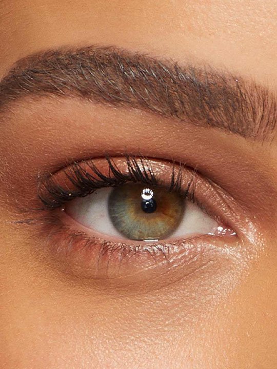 Nahaufnahme eines Auges mit natürlichem Make-up, dezent geschwungenen Wimpern und einer zweifarbigen Iris.
