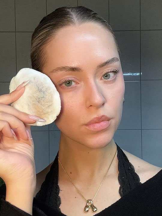 Junge Frau mit zurückgebundenem Haar entfernt ihr Augen-Make-up mit einem Wattepad – frischer, natürlicher Look im Badezimmer.