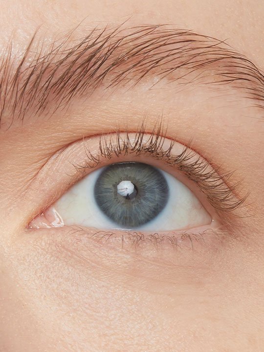 Makroaufnahme eines hellblauen Auges mit definierter, ungeschminkter Wimpern- und Brauenpartie.