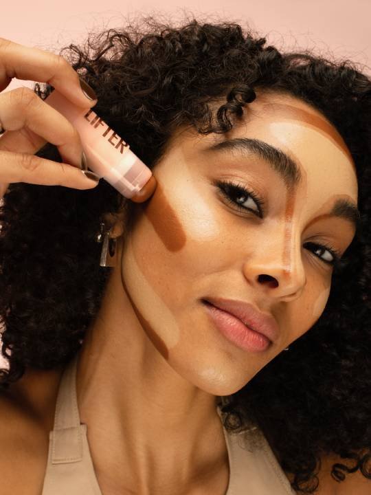 Nahaufnahme einer jungen, brünetten Frau, die mit einem Lifter-Stick Contouring auf ihr Gesicht aufträgt