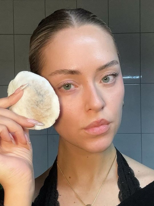 Blonde Frau reinigt ihr Gesicht sanft mit einem Wattepad.