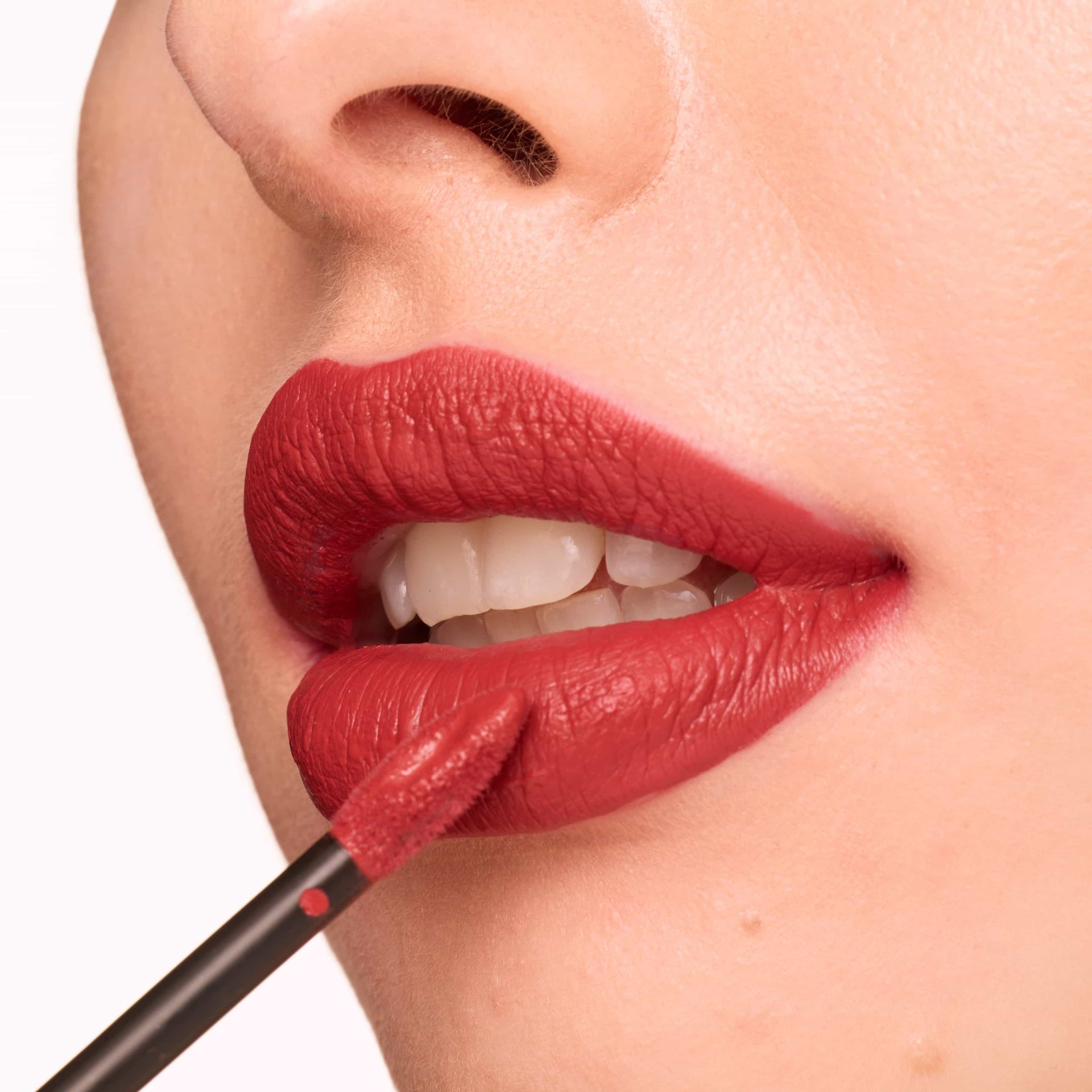 Nahaufnahme einer Frau, die sich ihre Lippen mit rotem, matten Lipgloss schminkt