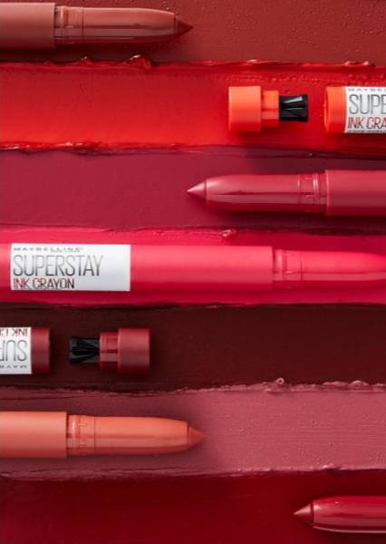 Verschiedene geöffnete Super Stay Ink Crayon Lippenstifte in Rot- und Brauntönen vor einem rotbraunen Hintergrund