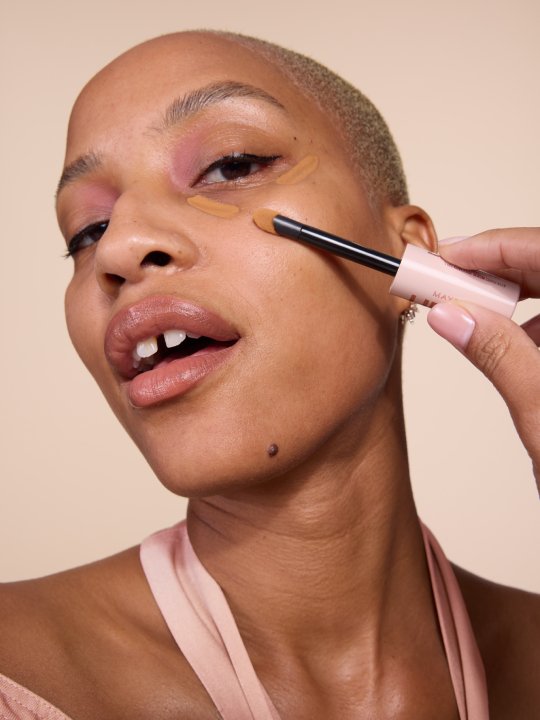 Nahaufnahme einer jungen Frau mit No Make-up Look, die Concealer unter ihren Augen aufträgt