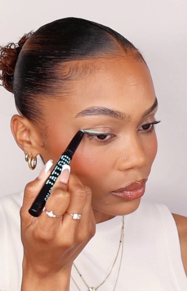 Eine Frau zieht sich mit einem grünen Eyeliner einen Lidstrich gezogen.