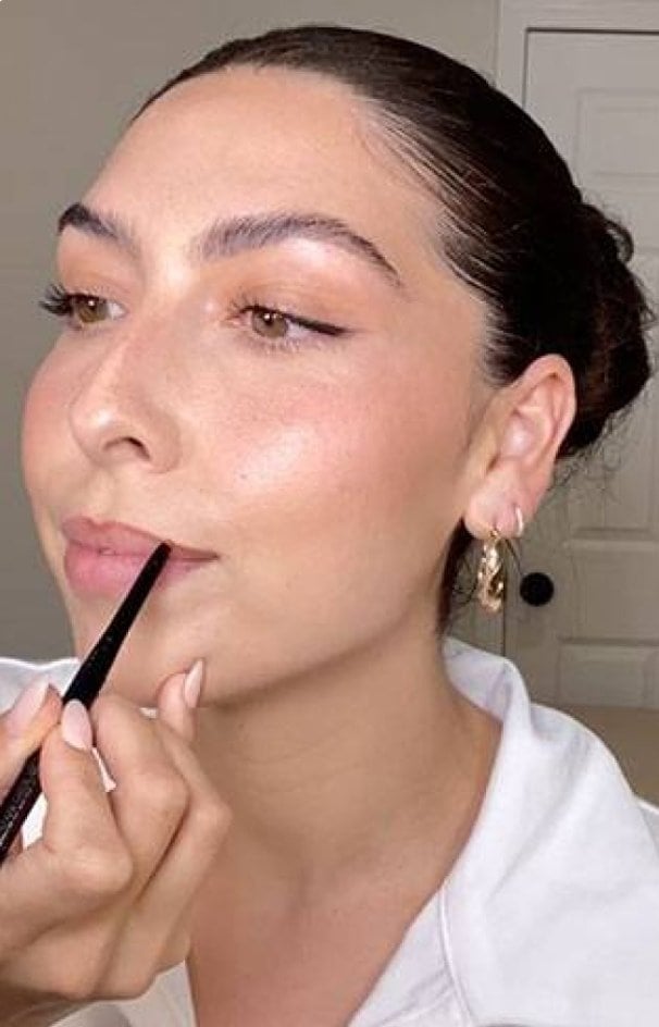 Eine Frau umrandet ihre Lippen mit einem Lipliner.