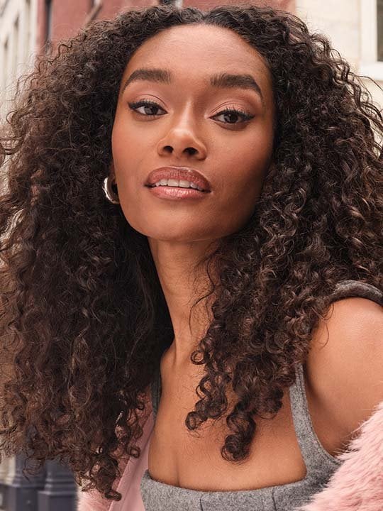 Model mit braunen langen Locken und einem ebenmäßigem Make-up-Look