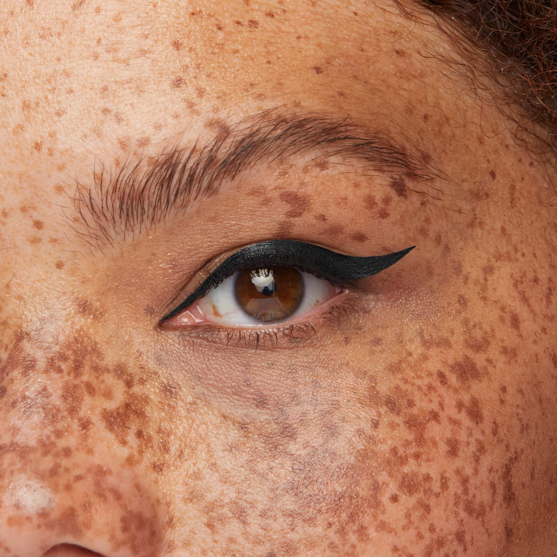 Auge einer Frau mit Sommersprossen und einem schwarzen gezogenen Eyeliner