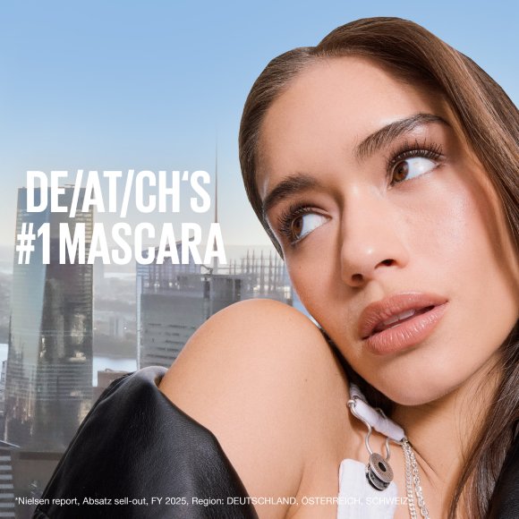 Ein Model mit perfekt definierten, langen Wimpern blickt nach oben vor einer hellblauen Stadtkulisse mit der Aufschrift „DE/AT/CH's #1 Mascara“.