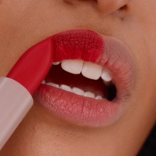 Nahaufnahme einer jungen Frau, die sich ihre Lippen mit einem roten Lippenstift schminkt
