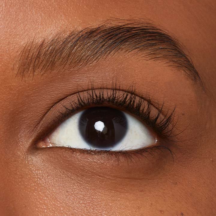 Makroaufnahme eines dunklen Auges mit definierter Braue und natürlichen, leicht geschwungenen Wimpern.
