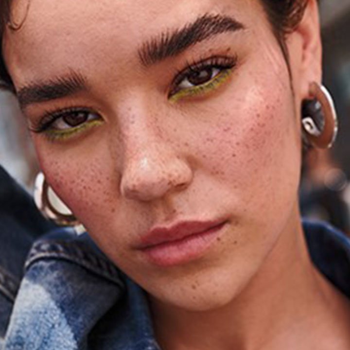 Porträt einer Frau mit buschigen, betonten Augenbrauen und auffälligem grünem Eyeliner – urbaner, selbstbewusster Street-Style-Look.
