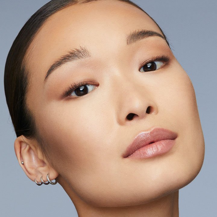 Porträtaufnahme einer Frau mit glänzendem Lippen-Make-up und definierten, natürlich gestylten Augenbrauen – minimalistischer Beauty-Look.