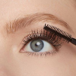 Nahaufnahme eines Auges einer jungen Frau, die Mascara auf ihre Wimpern aufträgt